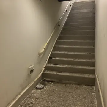 Fire extinguisher cabinet in Sublevel utility stairwell. The cabinet door is slightly ajar, revealing an incorrect type of hose. Yellowed caution tape
