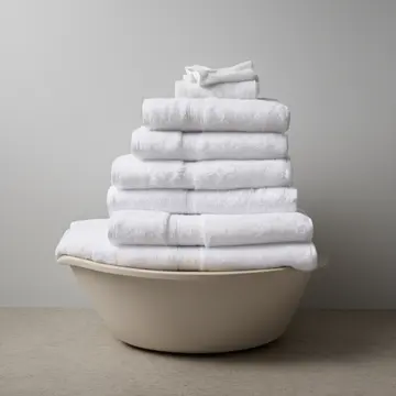 A stack of freshly folded white towels in Utility laundry room corner. The folding process has been interrupted and left unfinished. Lint caught on a dryer vent grate