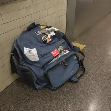 Overstuffed commuter backpack in Subway transfer vestibule. The bag is placed on a bench, slightly askew from its previous position. Wet vinyl bench surface