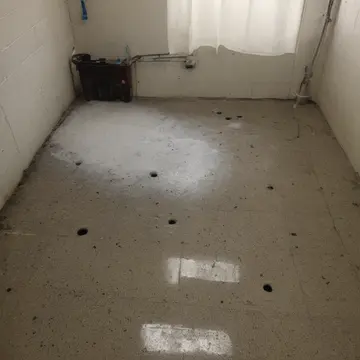 Overfilled soap dispenser in Laundromat utility room. The machine is leaking a thin, iridescent film onto the concrete floor. Soap residue streaks on tile grout