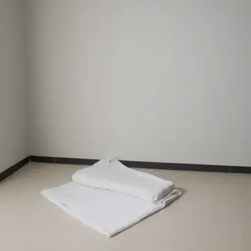 Folded stack of white towels in Laundry room corner. The routine folding process is interrupted by an unusual pattern on one towel. Damp lint buildup on the floor