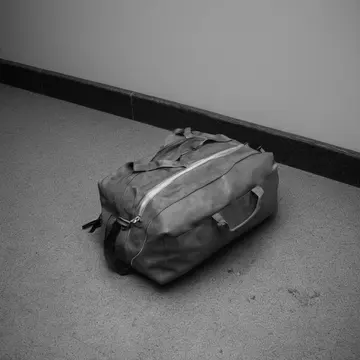 Overstuffed duffel bag in Bus terminal waiting area. A routine boarding check is interrupted by an unexpected weight shift. Scuffed linoleum floor