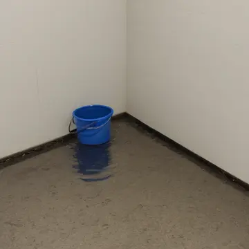 Mop bucket in Janitorial supply room corner. Water is still, reflecting the empty, polished floor. Wet linoleum tiles
