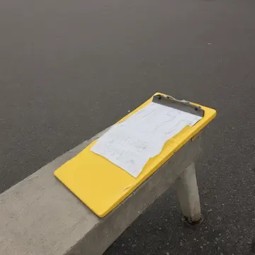 Clipboard with blank lines in Bus terminal waiting area. A small stack of forms is being checked for completeness. Yellow plastic clipboard