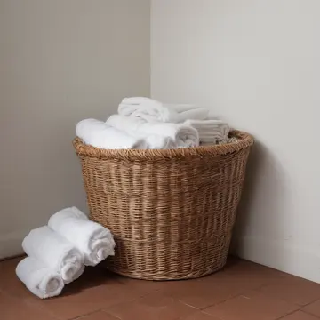 Overstuffed wicker laundry basket in Utility room near laundromat. Folding towels in low light. Lint caught on wicker spokes