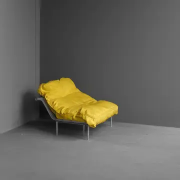 Single vinyl seat cushion in Public transit waiting area bench. A person is sitting alone, checking their phone for a delayed train. Scuffed yellow vinyl seams