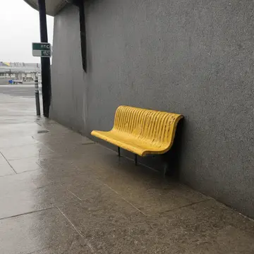 Empty plastic bench in Station corner shelter. Waiting for an unseen arrival in a quiet, regulated space. Yellow faded plastic slats