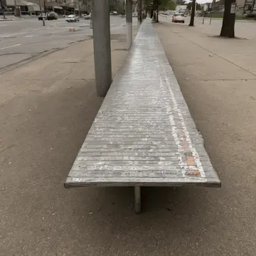 Wet plastic bench seat in Station corner shelter. Waiting for the 41 bus, people are stacking and rearranging discarded newspapers. Faded vinyl bench slats