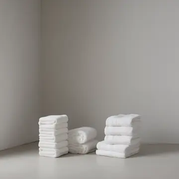 Stacked linen towels in Utility sink corner. A small pile of freshly folded, damp linens is being arranged for storage. Slight sheen of soap residue on porcelain