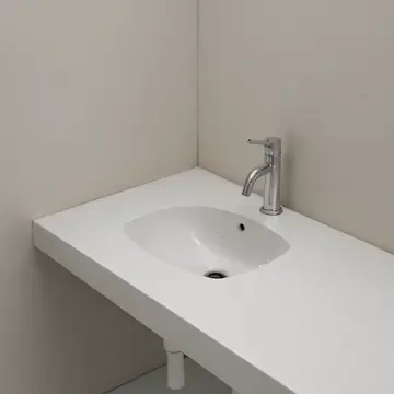 Industrial porcelain sink basin in Utility closet near public washrooms. A damp, unused corner of the sink holds a single, misplaced object. Water spots on chrome faucet base
