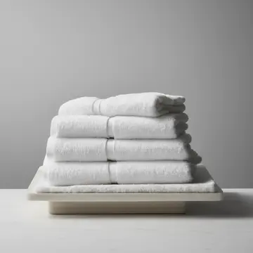 Stack of folded white towels in Utility sink area. A person is carefully folding and stacking clean linens, but the stack keeps shifting slightly. Slightly damp steam rising