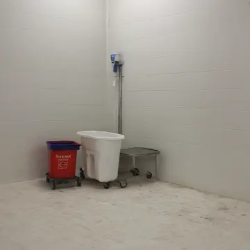 Mop bucket and discarded cleaning supplies in Retail storeroom corner. The mop water reflects the empty, polished floor. Wet tile sheen