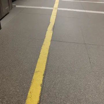 The discarded fare card reader in Suburban bus terminal bench. A small section of the platform floor is taped off for 'inspection'. Yellow tape barrier