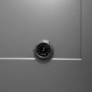 Industrial freezer unit in Service corridor behind a dry cleaner. The door seals, but an internal light source remains faintly visible. Sweat residue on stainless steel handle