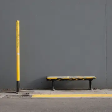 Metal coat hook in Station corner bus shelter. Midday waiting period; routine maintenance is underway on the adjacent utility box. Yellow warning tape
