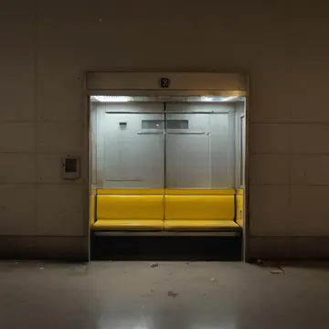 Rubber doorstop in Station corner waiting booth. Morning reset before commuter rush. Yellow faded timetable board