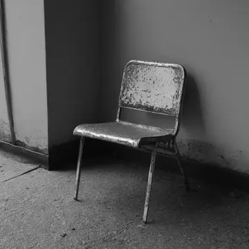 Folding chair in Bus shelter corner. The chair repeatedly shifts slightly off its marked spot. Wet asphalt stains