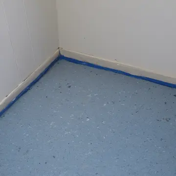 Stacked cardboard boxes in Utility closet off laundry room. A damp patch is spreading across the linoleum floor. Salt stains on grout